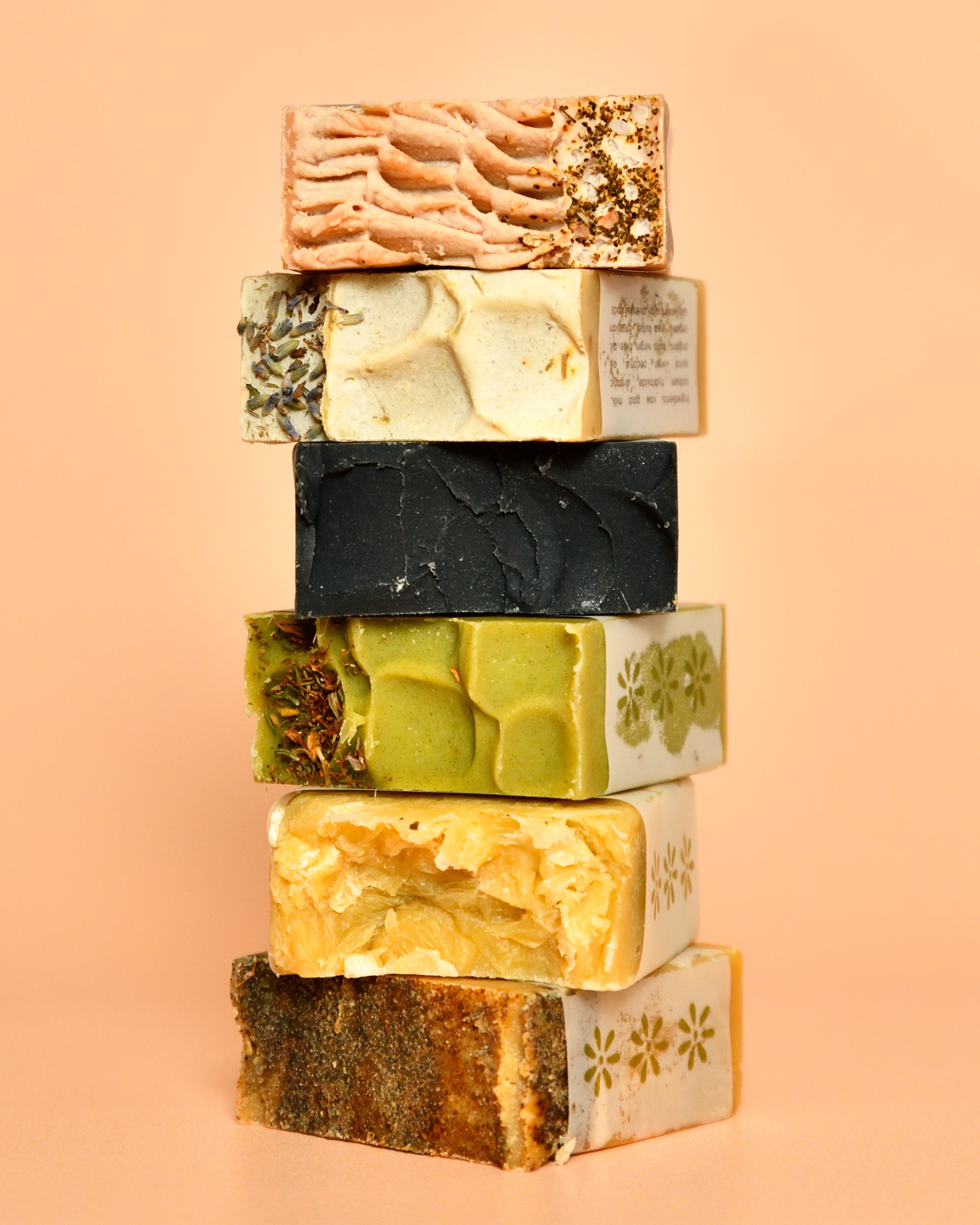 A stack of various Goat Milk Bar Soaps with different colors and patterns on a pale orange background.