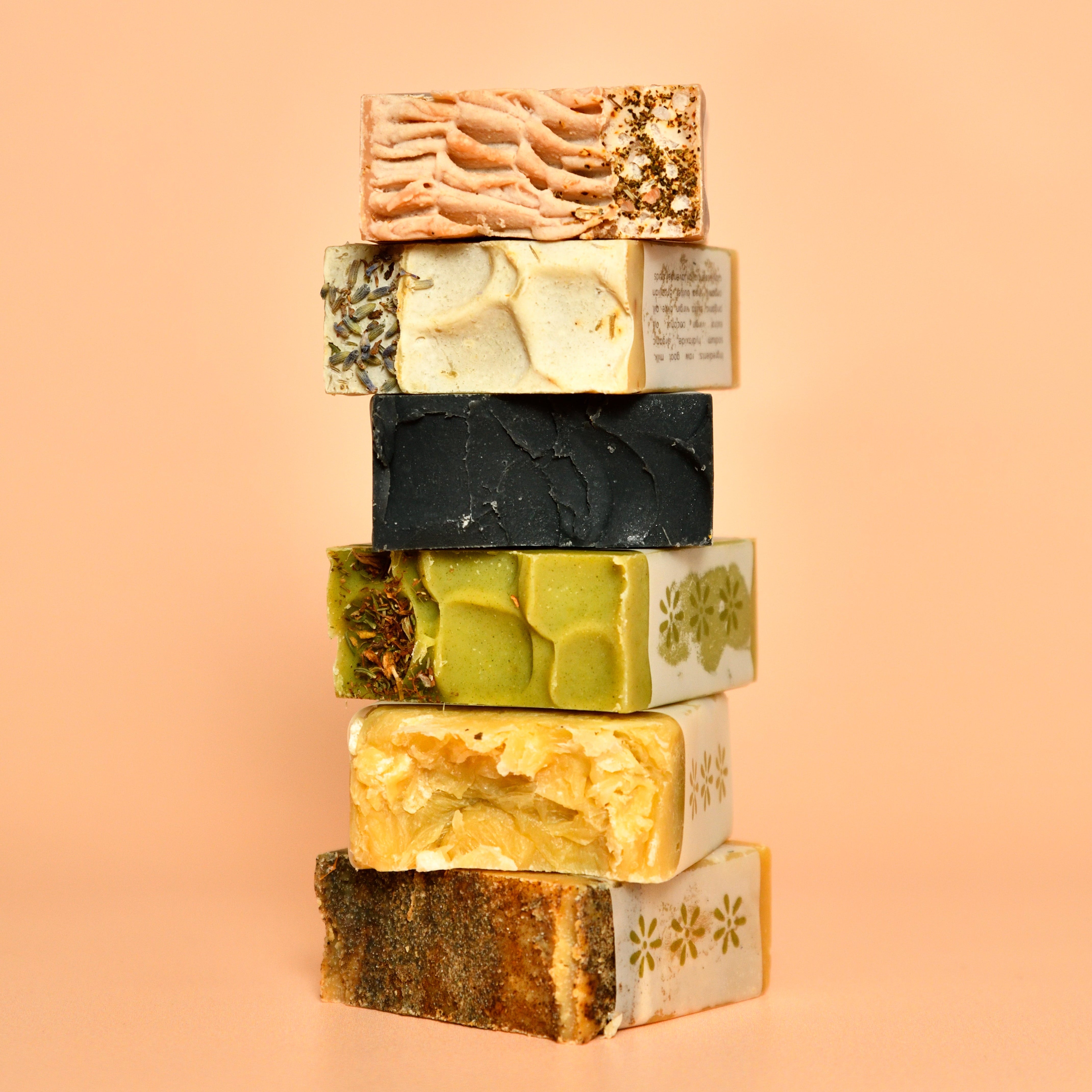 A stack of various Goat Milk Bar Soaps with different colors and patterns on a pale orange background.
