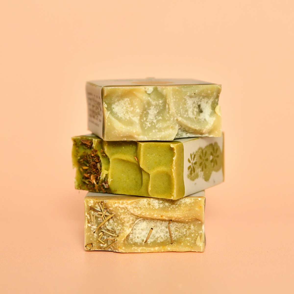 Three bars of goat milk soap with a golden hue and floral patterns on top, stacked on a pink background.