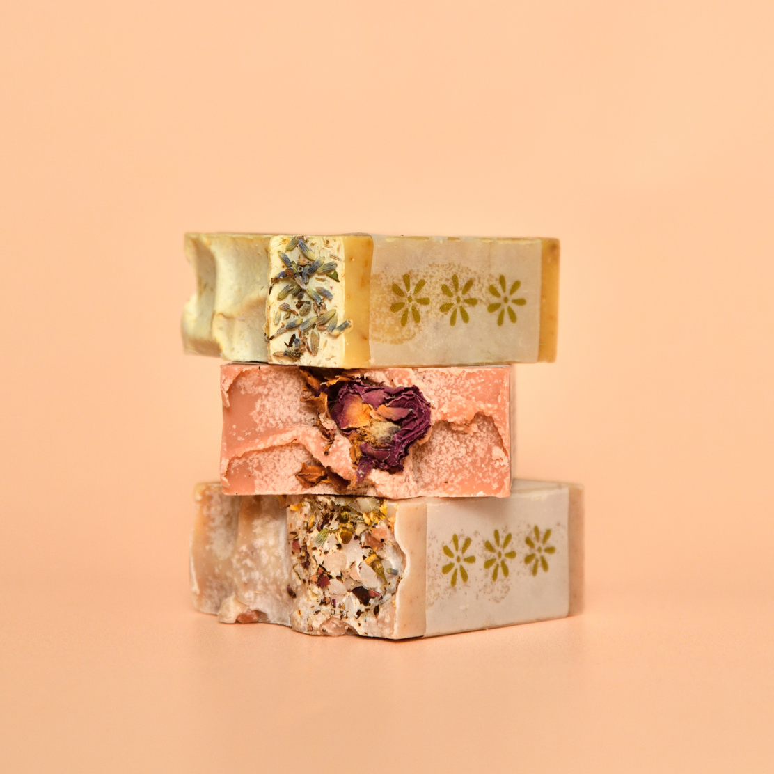 Three stacked soap bars with natural ingredients on a peach background