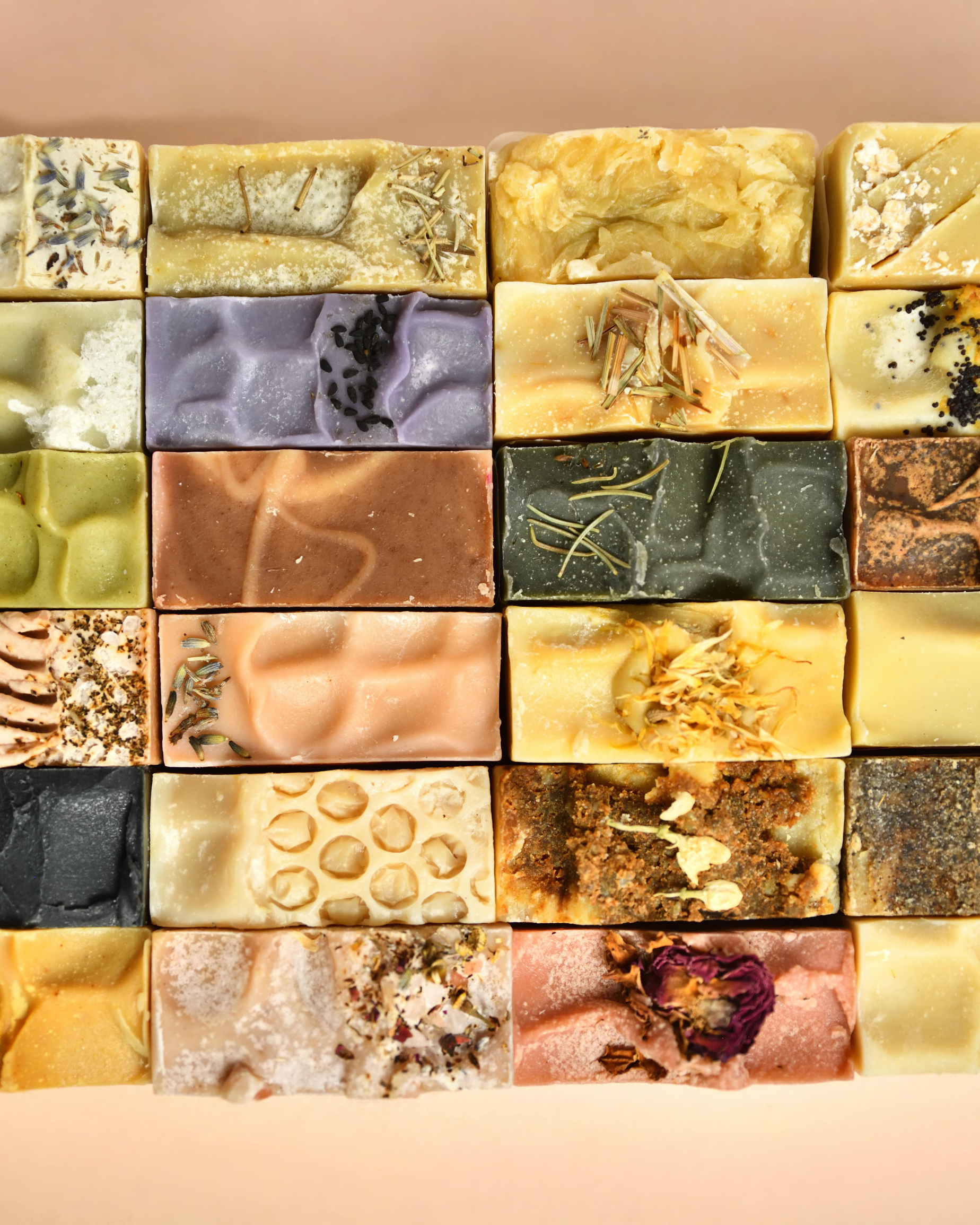 Collection of variously textured and colored soap tops arranged in a grid on a peach background.