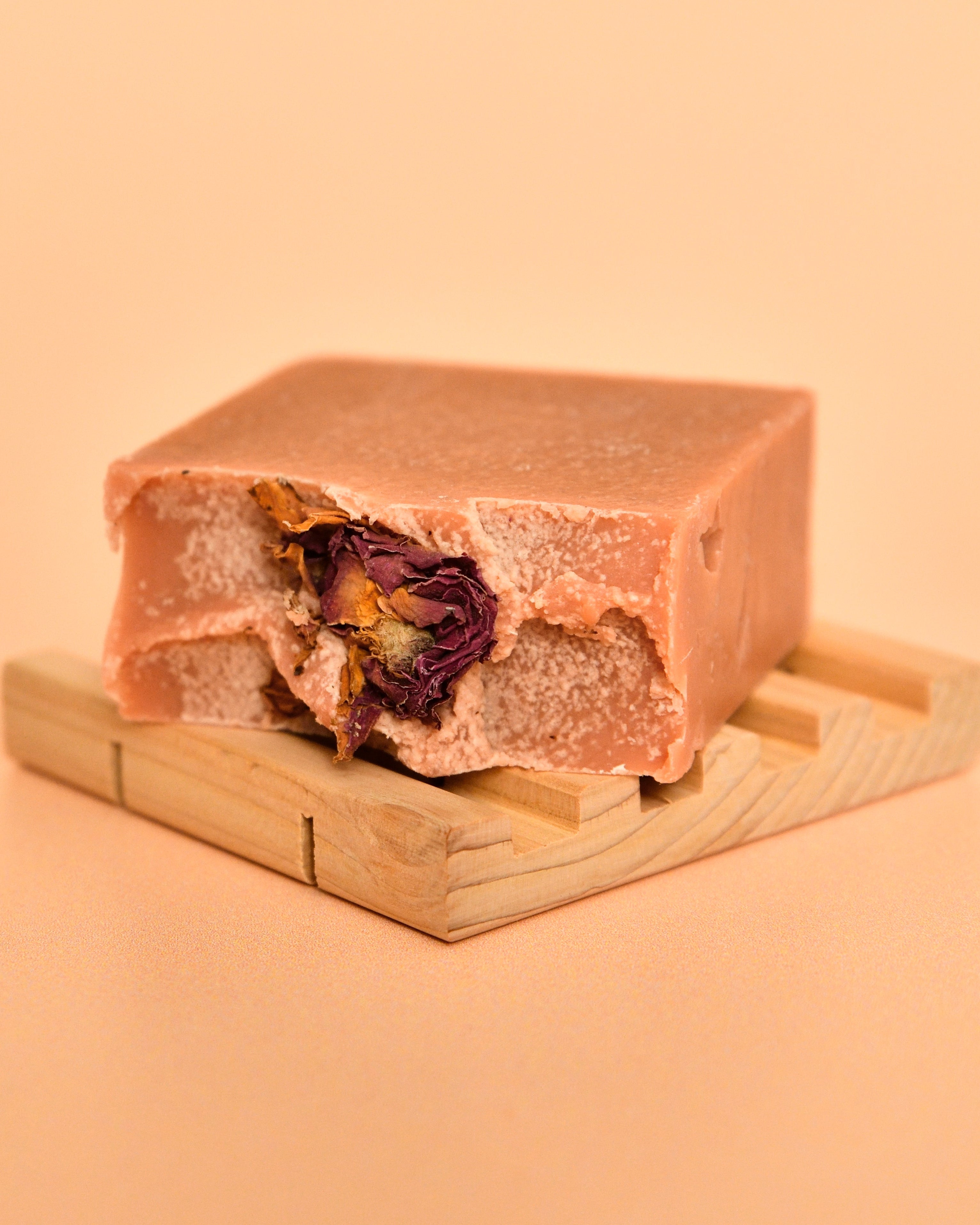 Bar of soap with a visible flower inside on a wooden stand against a beige background