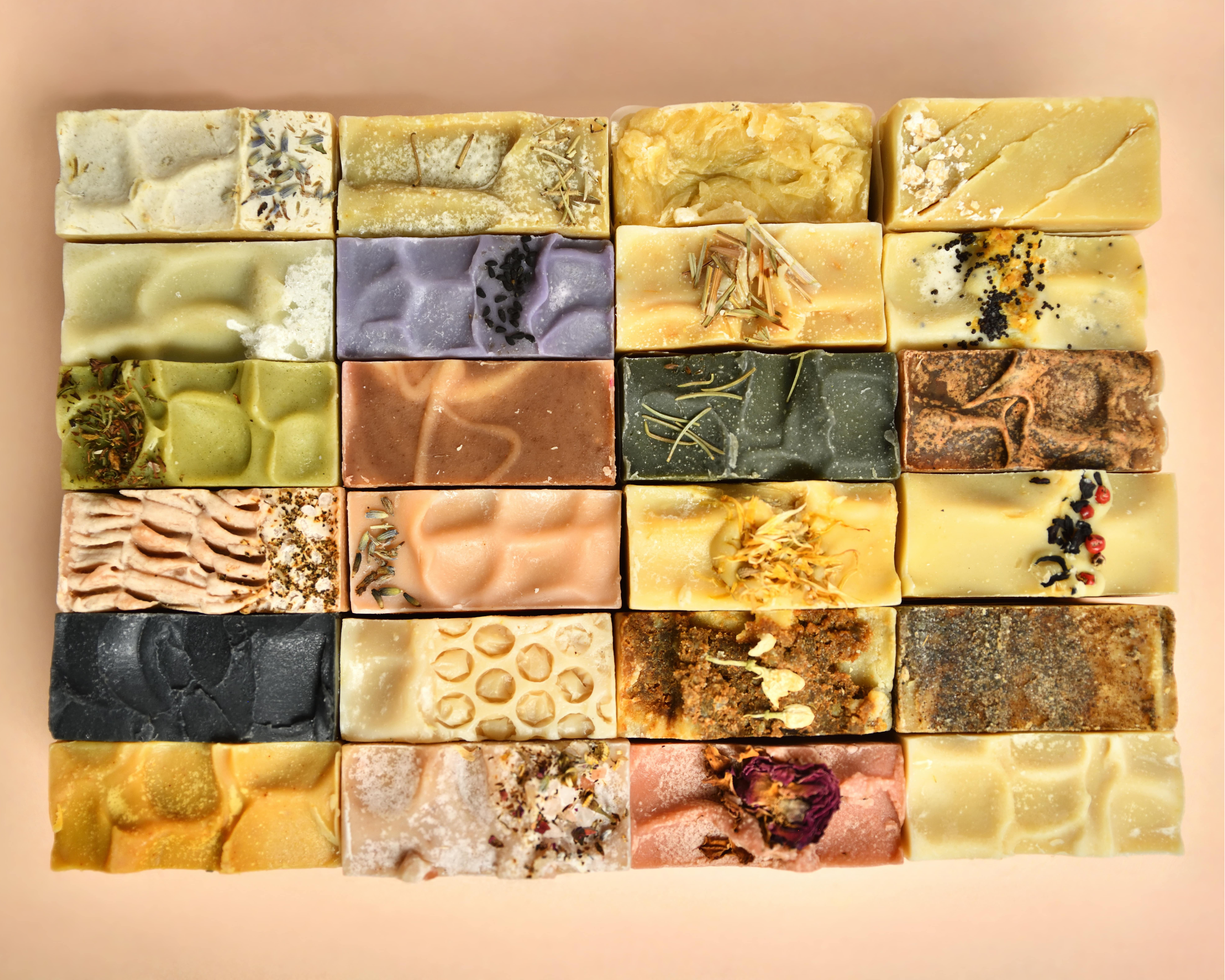 Collection of variously textured and colored soap tops arranged in a grid on a peach background.