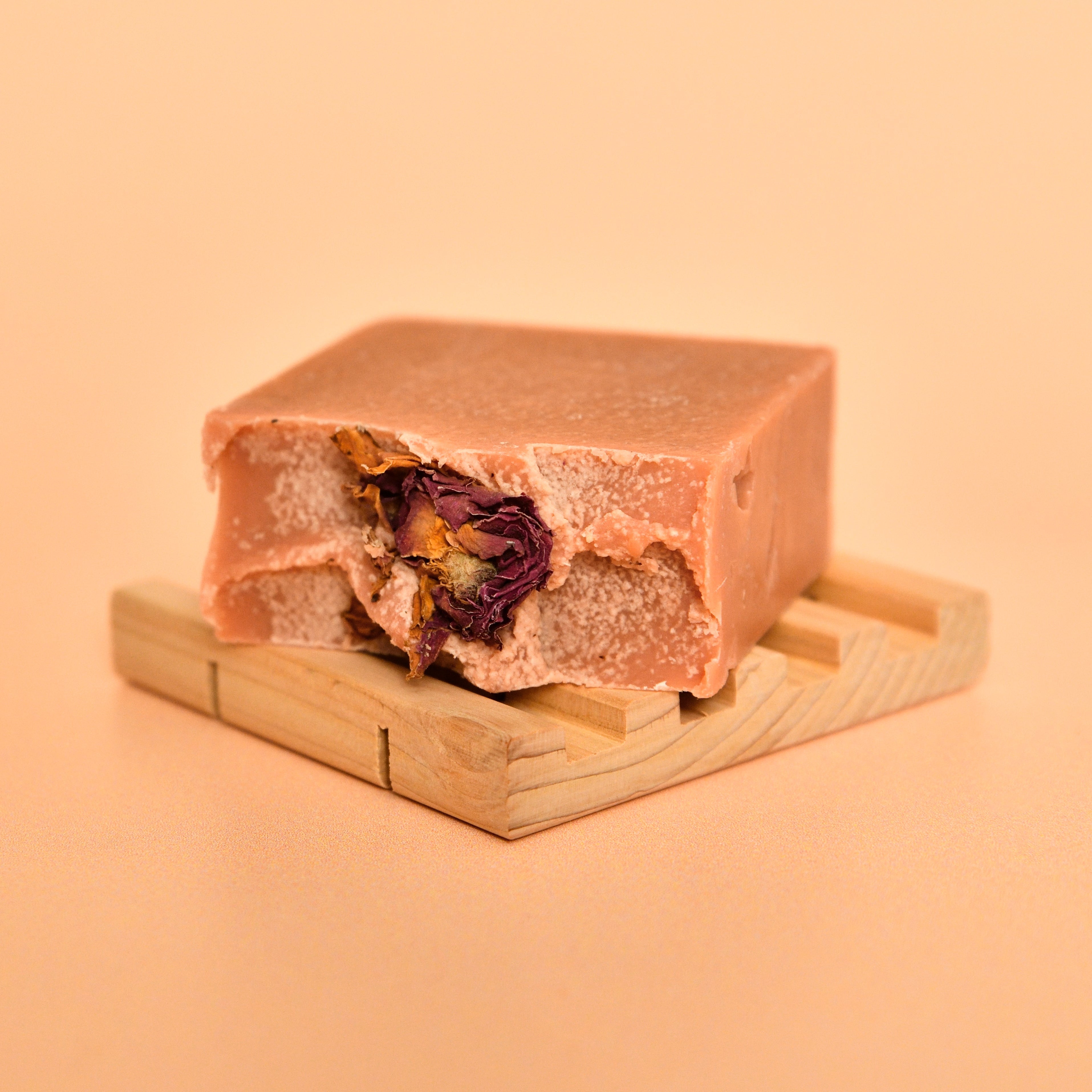 Bar of soap with a visible flower inside on a wooden stand against a beige background